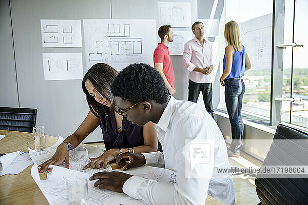 Männlicher und weiblicher Architekt diskutieren über Geschäftsplan mit Blaupause am Konferenztisch im Sitzungssaal