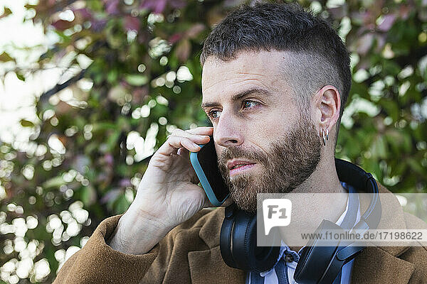 Mid adult businessman wearing headphones talking on mobile phone standing outdoors