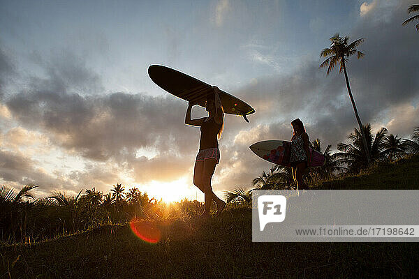 Zwei Frauen mit Surfbrettern auf einem Hügel bei Sonnenuntergang auf der Insel Siargao  Philippinen