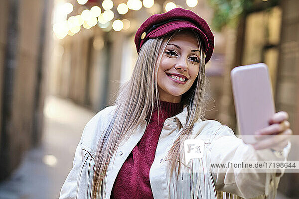 Lächelnde schöne Frau trägt flache Kappe unter selfie durch smart phone