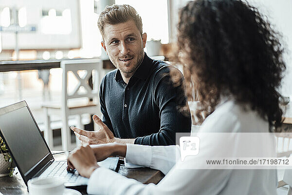 Businessman having discussion with colleague using laptop while sitting at cafe