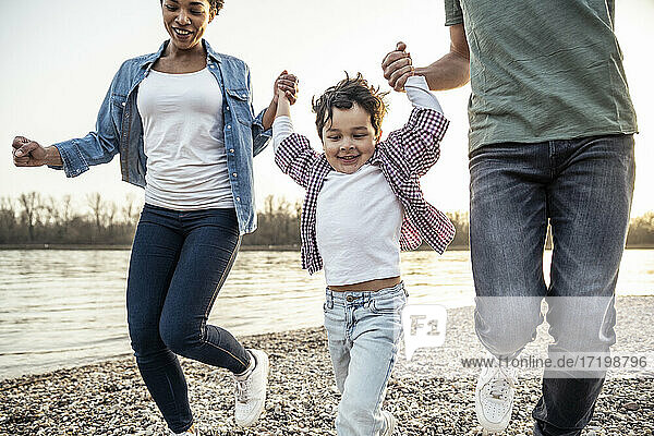 Verspielte Familie  die sich beim Laufen am See an den Händen hält