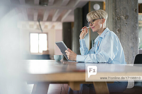 Smiling businesswoman using digital tablet while sitting at desk in home office