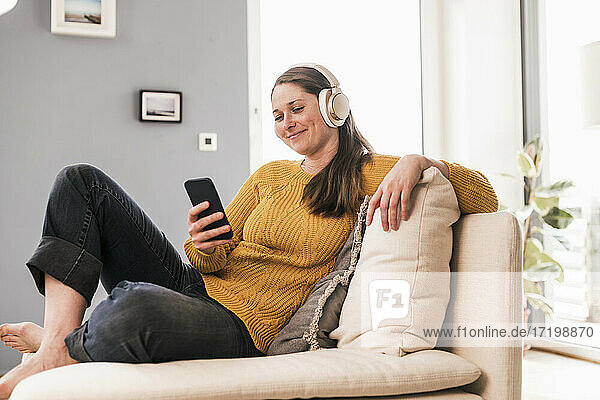 Lächelnde Frau mittleren Alters  die zu Hause Musik über Kopfhörer hört