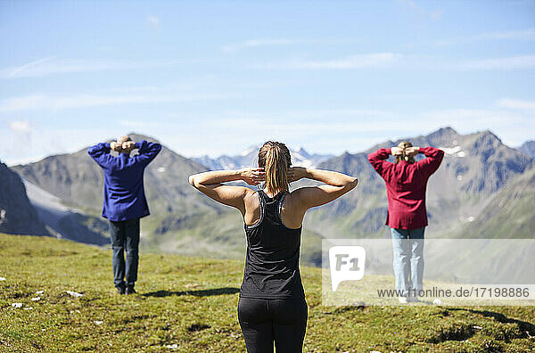 Kaukasischer Mann und Frauen mit Händen hinter dem Kopf üben vor einem Berg