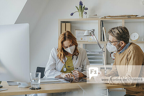Arzt und Patient benutzen ein digitales Tablet  während sie in der Arztpraxis sitzen