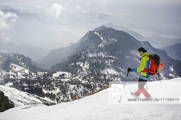 Männlicher Wanderer mit Rucksack und Wanderstock auf einem schneebedeckten Berg  der Steigeisen trägt