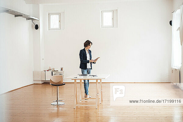 Businesswoman using digital tablet in front of white wall at home office