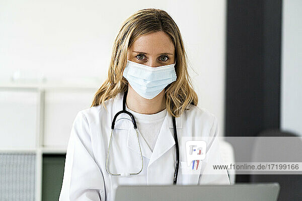 Blond female medical worker with laptop working at medical clinic during COVID-19