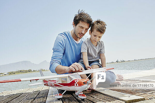 Reifer Mann und Junge unterhalten sich  während sie ein Spielzeugflugzeug auf einem Pier berühren