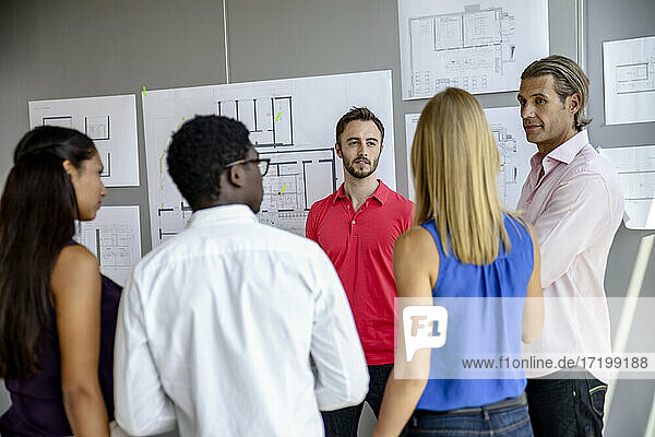 Geschäftsmann  der mit Kollegen über die Planung diskutiert  während er im Büro vor einer weißen Tafel steht