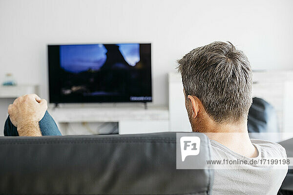 Man watching television while sitting on sofa in living room