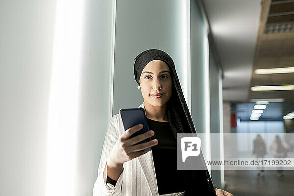 Junge arabische Frau  die ein Smartphone benutzt  während sie in der Nähe einer Wand in einer Einkaufsstraße steht