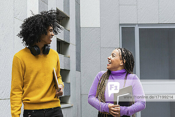 Lächelnde Studenten  die sich gegenseitig anschauen  während sie in der Universität stehen