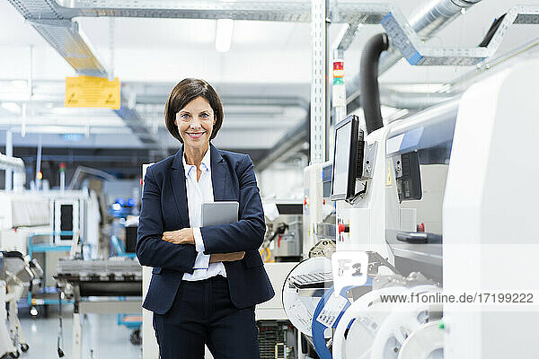 Selbstbewusste Geschäftsfrau mit digitalem Tablet an einer Maschine in einer Fabrik