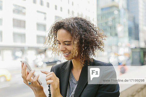 Lächelnde Afro-Geschäftsfrau mit Smartphone in der Stadt