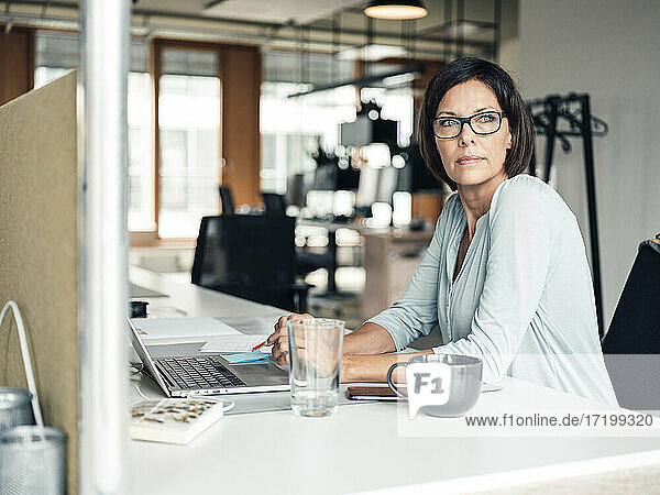 Selbstbewusste Unternehmerin mit Laptop  die am Schreibtisch im Büro wegschaut
