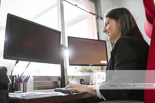 Lächelnde Geschäftsfrau  die einen Computer benutzt  während sie in einem Lagerbüro sitzt