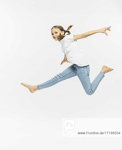 Mädchen mit ausgestreckten Armen gestikuliert beim Springen vor weißem Hintergrund