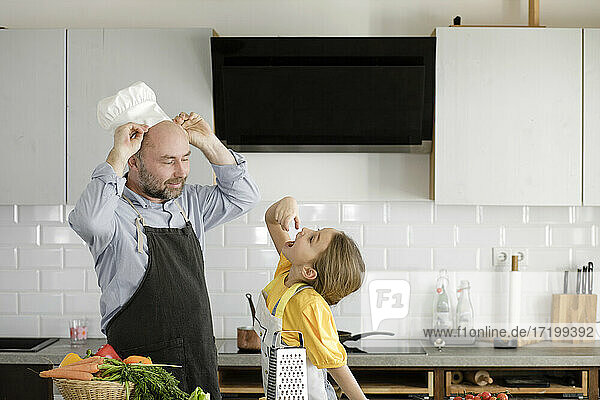 Vater trägt Kochmütze und steht bei seiner Tochter zu Hause