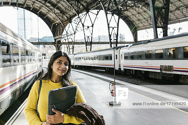 Mittlere erwachsene Frau mit Laptoptasche schaut weg  während sie auf dem Bahnsteig steht