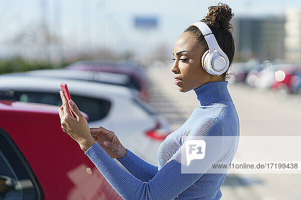 Junge Frau mit Kopfhörern  die ein Mobiltelefon benutzt  während sie auf einem Parkplatz steht