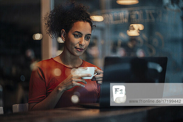 Junge Frau mit Kaffeetasse  die in einem Café sitzt und am Laptop arbeitet