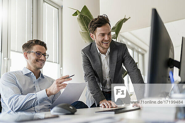 Lächelnde Geschäftsleute diskutieren über Computer am Schreibtisch im Büro