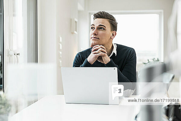 Thoughtful businessman with laptop looking away while sitting at desk