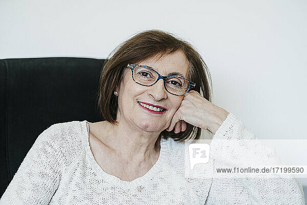 Lächelnde ältere Frau  die zu Hause an der Wand sitzt