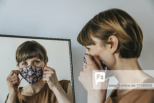 Brown haired woman wearing protective face mask while looking in mirror during pandemic