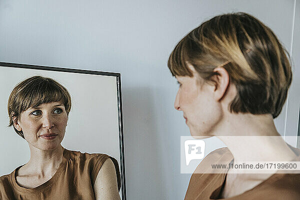 Nachdenkliche Frau betrachtet ihre Reflexion im Spiegel