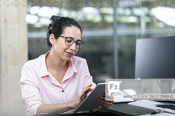 Unternehmerin  die ein digitales Tablet benutzt  während sie am Schreibtisch im Büro sitzt