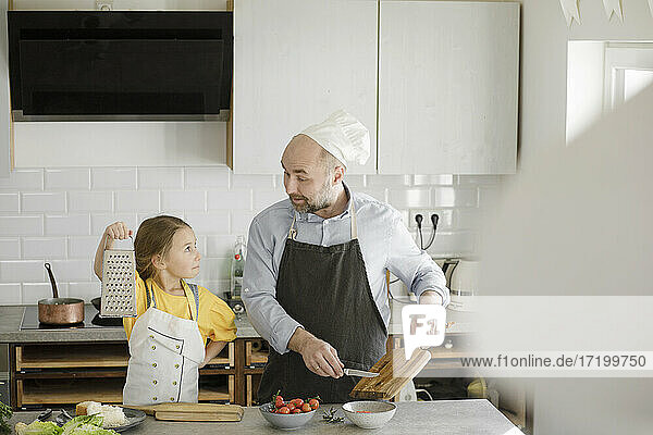 Mädchen zeigt dem Vater in der Küche zu Hause eine Reibe