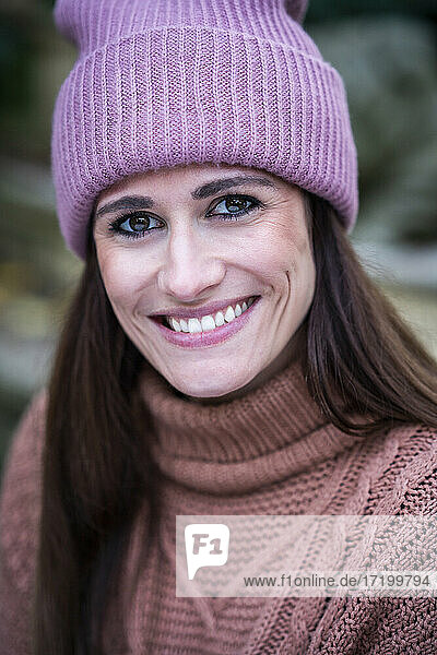 Porträt einer schönen Frau mit rosa Strickmütze  die in die Kamera lächelt