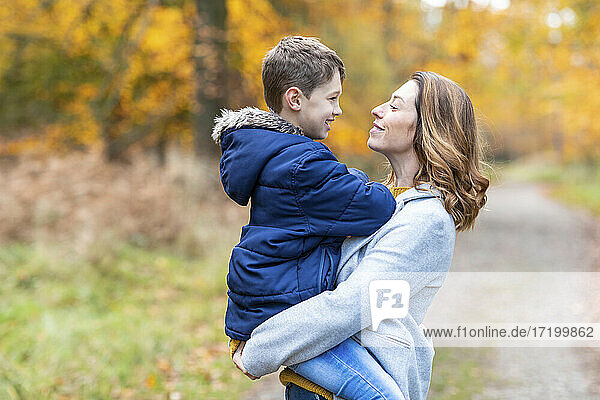 Mutter trägt lächelnden Sohn in den Armen  während sie im Wald steht