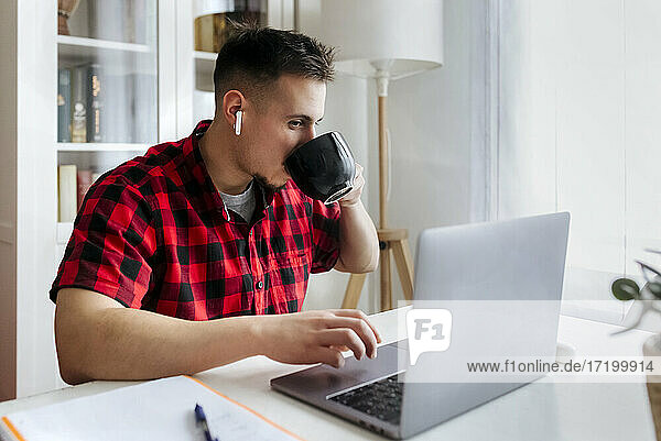 Geschäftsmann trinkt Kaffee  während er im Büro zu Hause am Laptop arbeitet