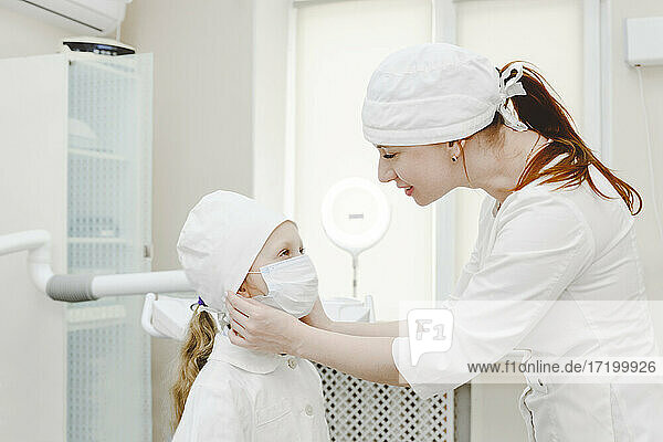 Female dentist putting on protective face mask on little girl