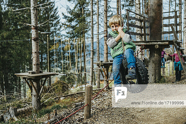 Boy swinging with rope on tire in forest at Salzburger Land  Austria