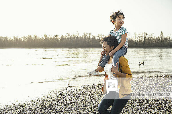 Young woman carrying boy on shoulders while running by lakeshore