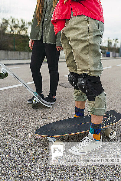 Woman with skateboard wearing protective kneepad while standing by female friend on road