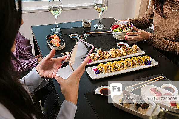 Women photographing food through mobile phone while sitting with female friends at restaurant
