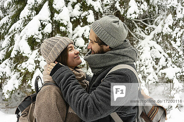 Couple wearing warm clothing looking at each other while standing in forest