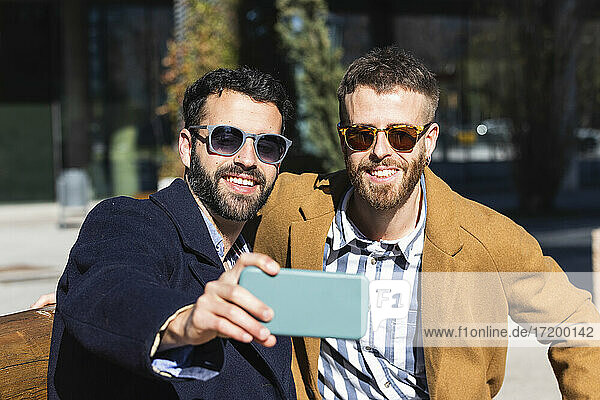 Lächelnde Geschäftspartner  die ein Selfie mit ihrem Mobiltelefon machen  während sie im Freien sitzen