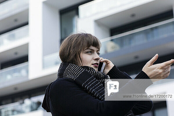 Frau gestikuliert  während sie mit einem Mobiltelefon spricht  das an einem Gebäude steht