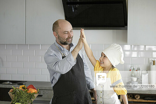 Smiling father and daughter giving high-five while standing at kitchen