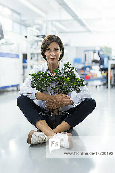 Mature female entrepreneur embracing potted plant sitting in laboratory