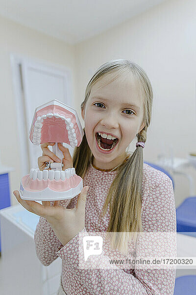 Portrait of little blonde girl standing in dentists office with dentures in hands