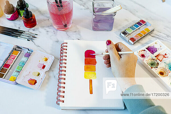Frau malt Popsickle-Eis mit Aquarellfarbe in einem Buch auf dem Tisch