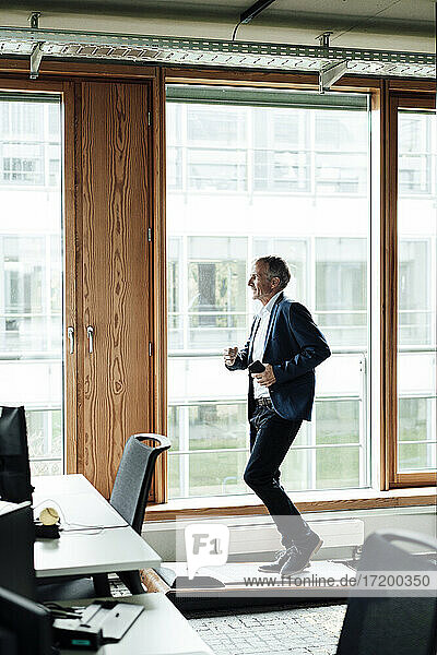 Senior businessman with mobile phone exercising on treadmill in office